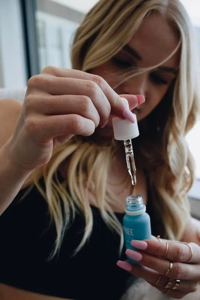 A woman with blonde hair using a dropper to transfer liquid from a small bottle into a blue container.