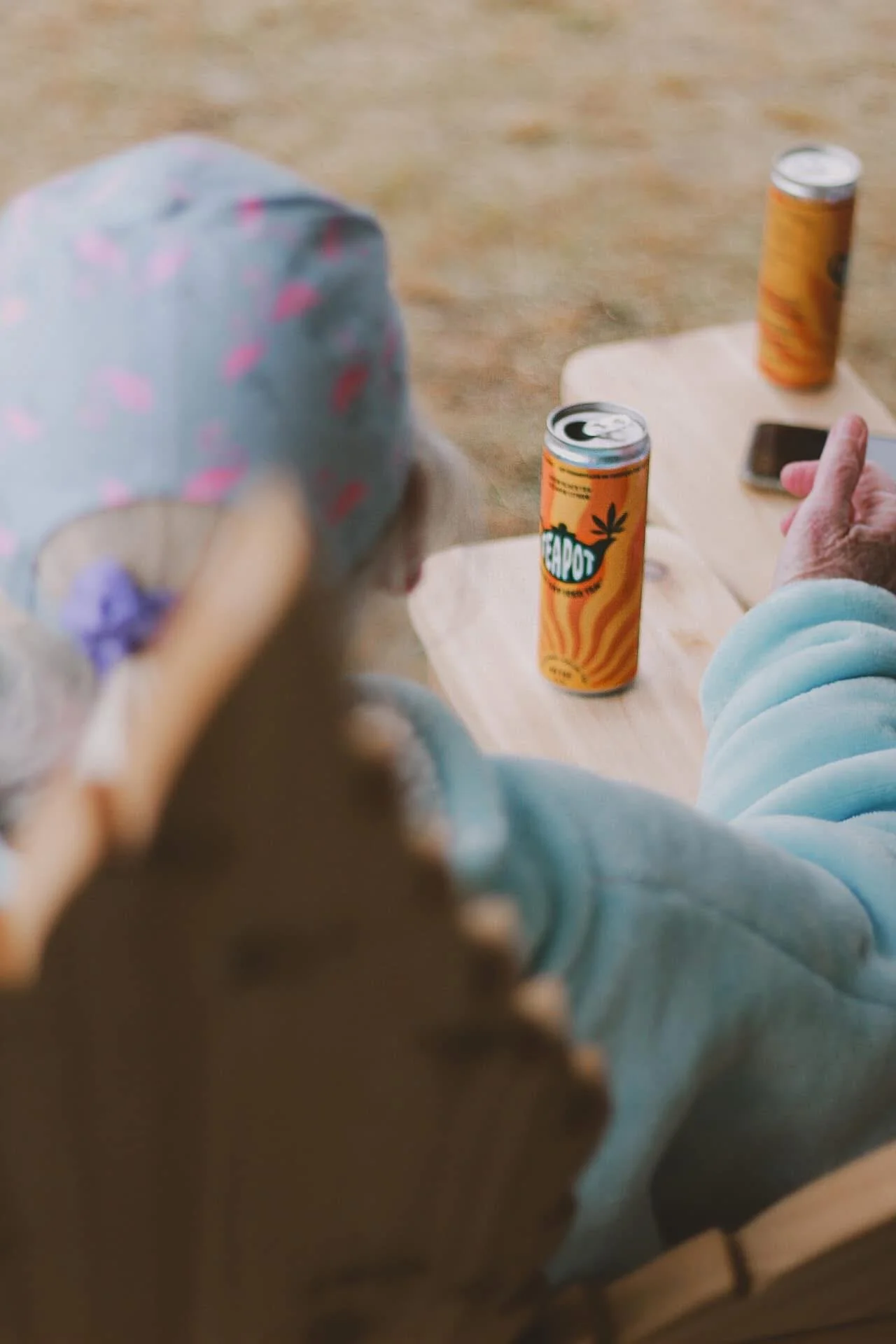 View of two orange cans on a wooden table with a person in a light blue sweatshirt sitting nearby, holding a small item in their hand.