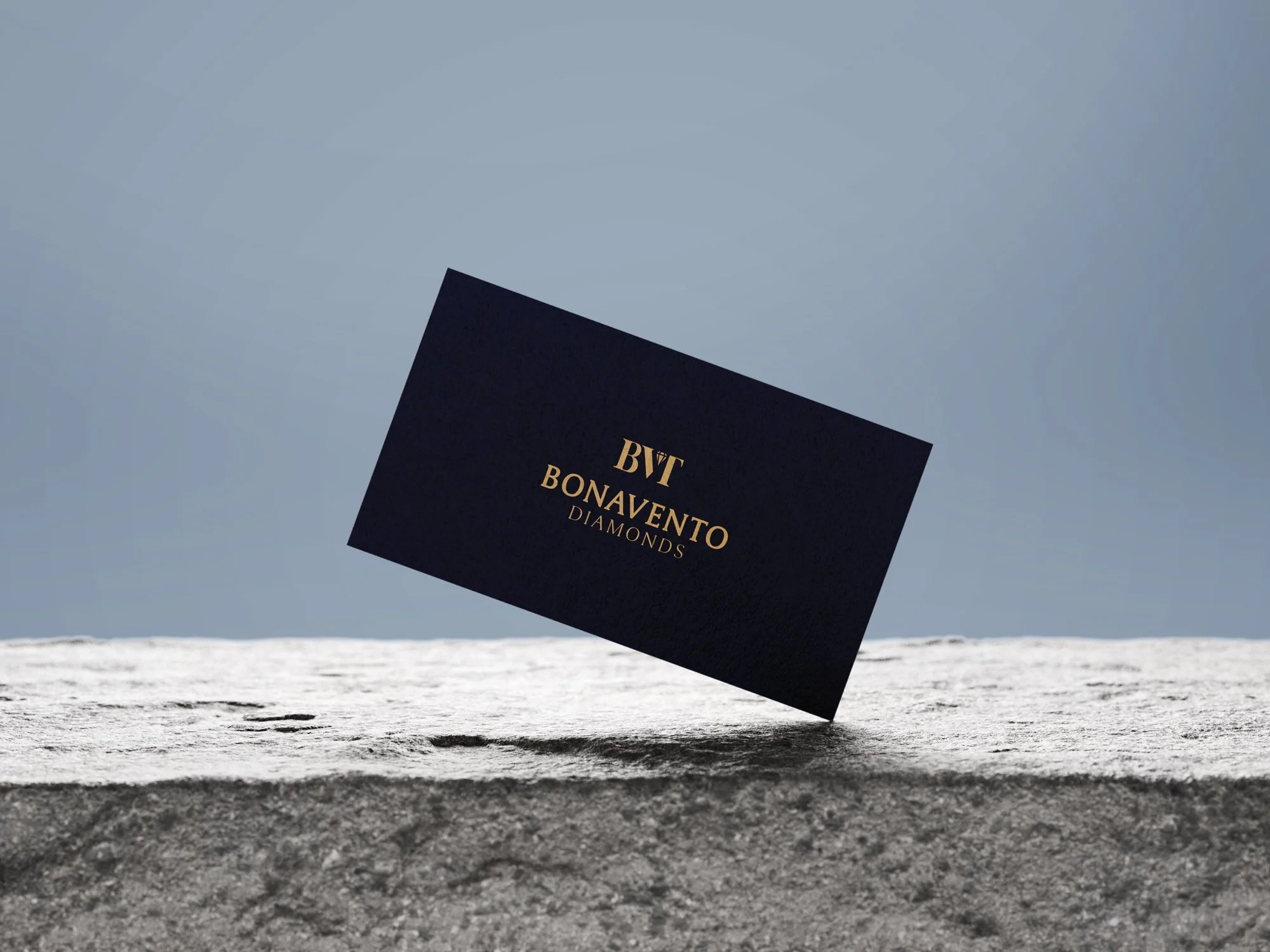 Black card with gold text reading 'BVT BONAVENTO DIAMONDS' floating above a sandy beach with a gray sky in the background.
