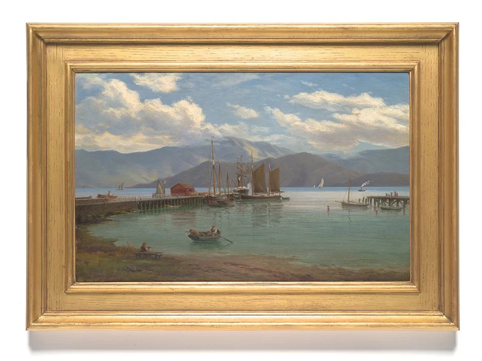 A framed landscape painting of a harbor with ships, mountains in the background, and a partly cloudy sky. Akaroa Museum Collection