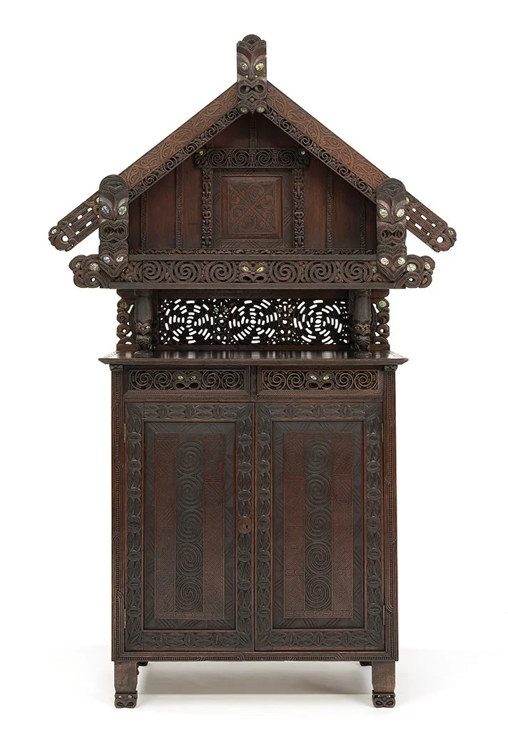 Intricately carved wooden cabinet with a house-like top featuring detailed patterns and scrollwork. Akaroa Museum Collection.