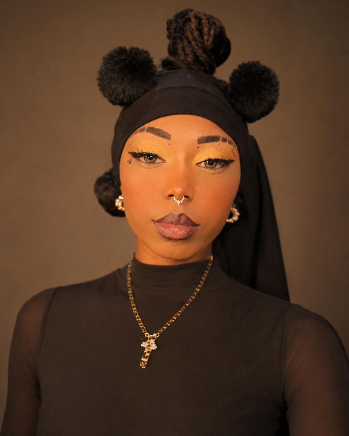 Portrait of a woman with styled hair, gold makeup, earrings, a nose piercing, and wearing a black headscarf with pom-pom decorations, in a black top, against a neutral background.