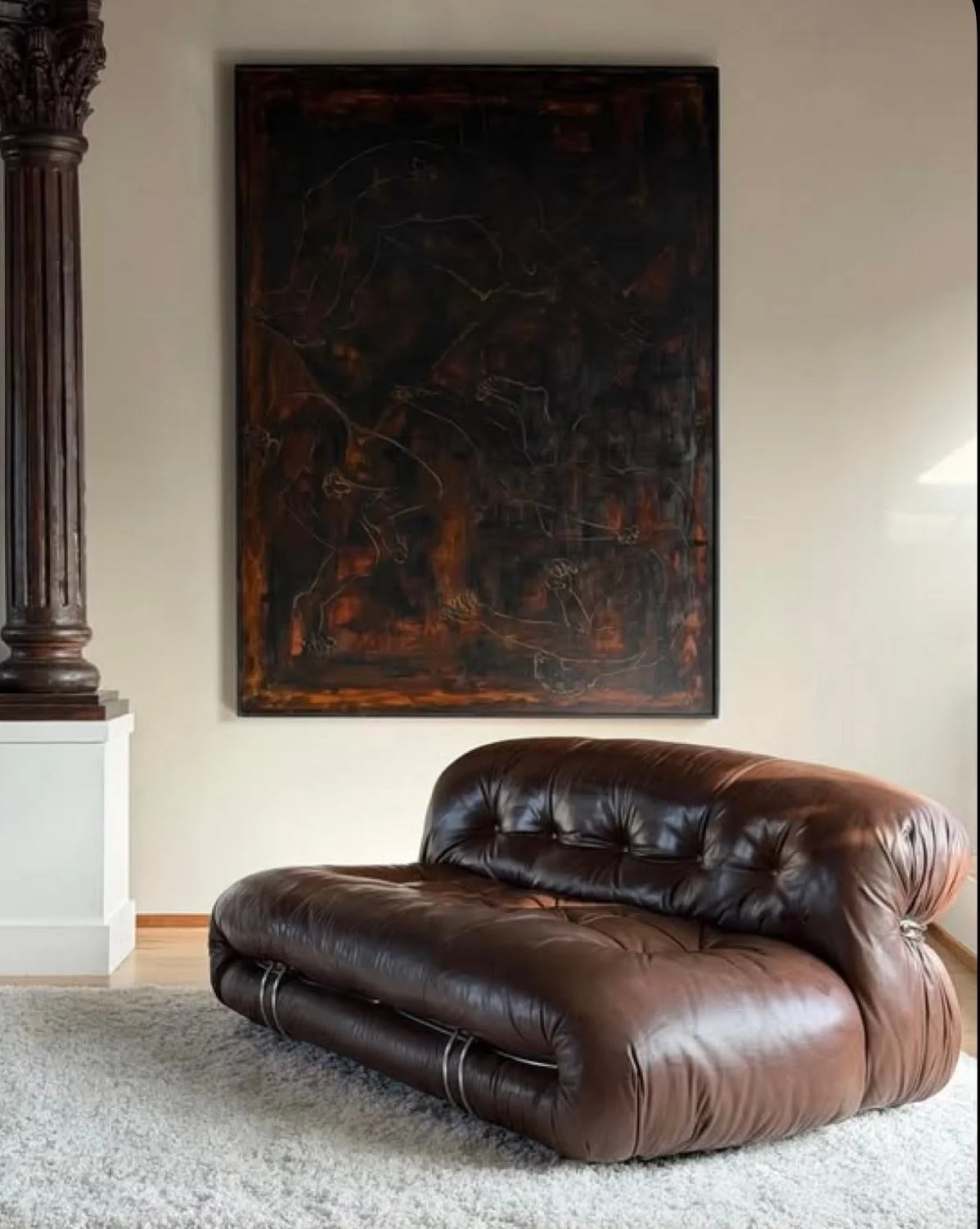 A living room with a dark leather couch, a large wall art piece behind it, and a white wall on the right side of the image.