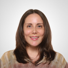 A woman with shoulder-length brown hair, smiling, wearing a multicolored top against a light gray background.
