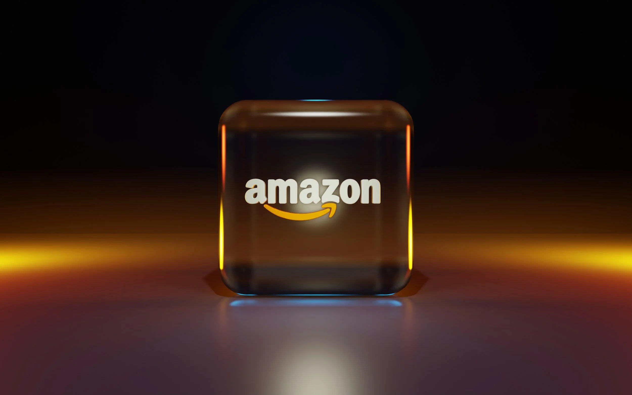 A glass cube with the Amazon logo illuminated on it, set against a dark background with colorful lighting effects.
