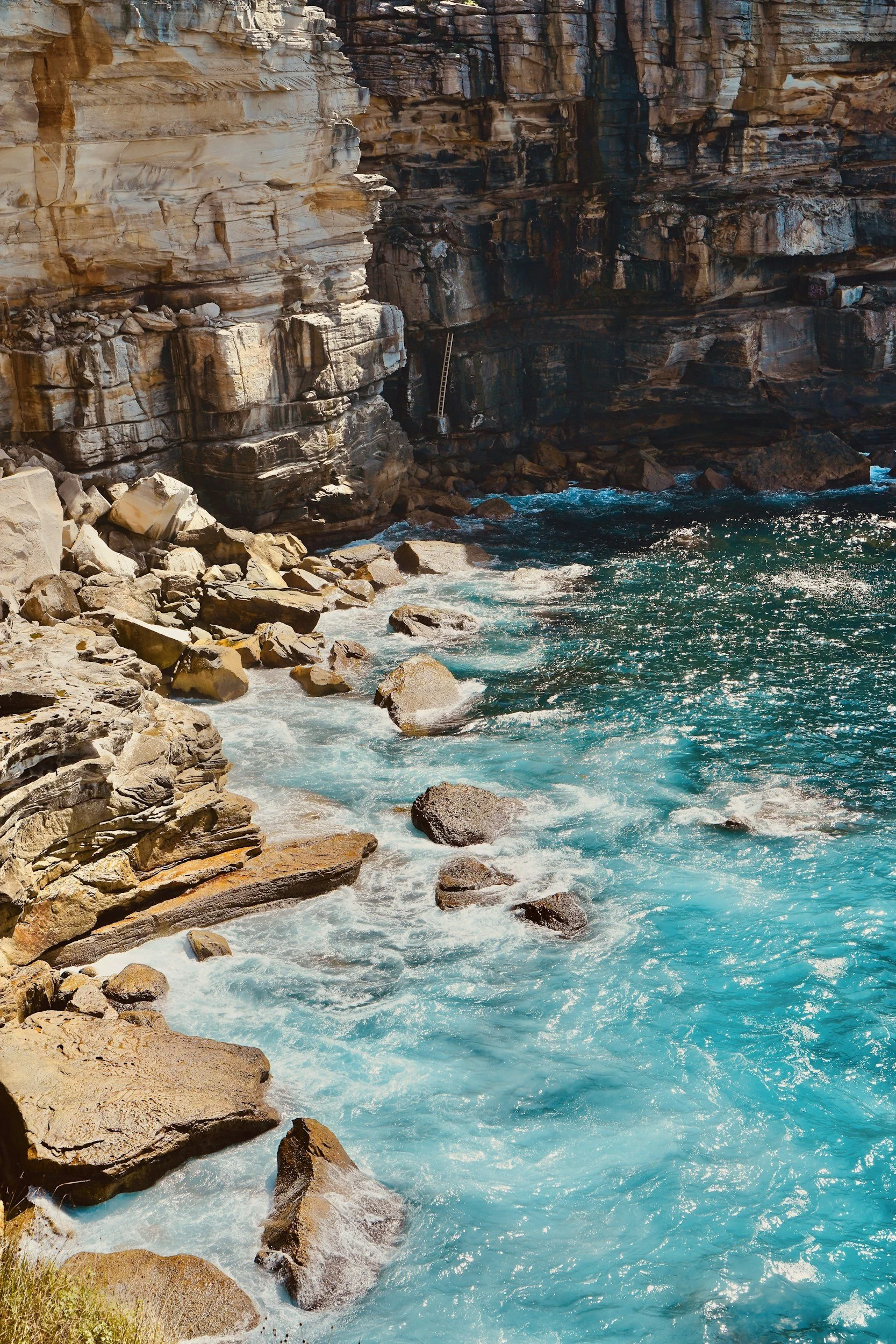 Rocky canyon with blue water rushing at the bottom and a ladder leaning against the canyon wall.