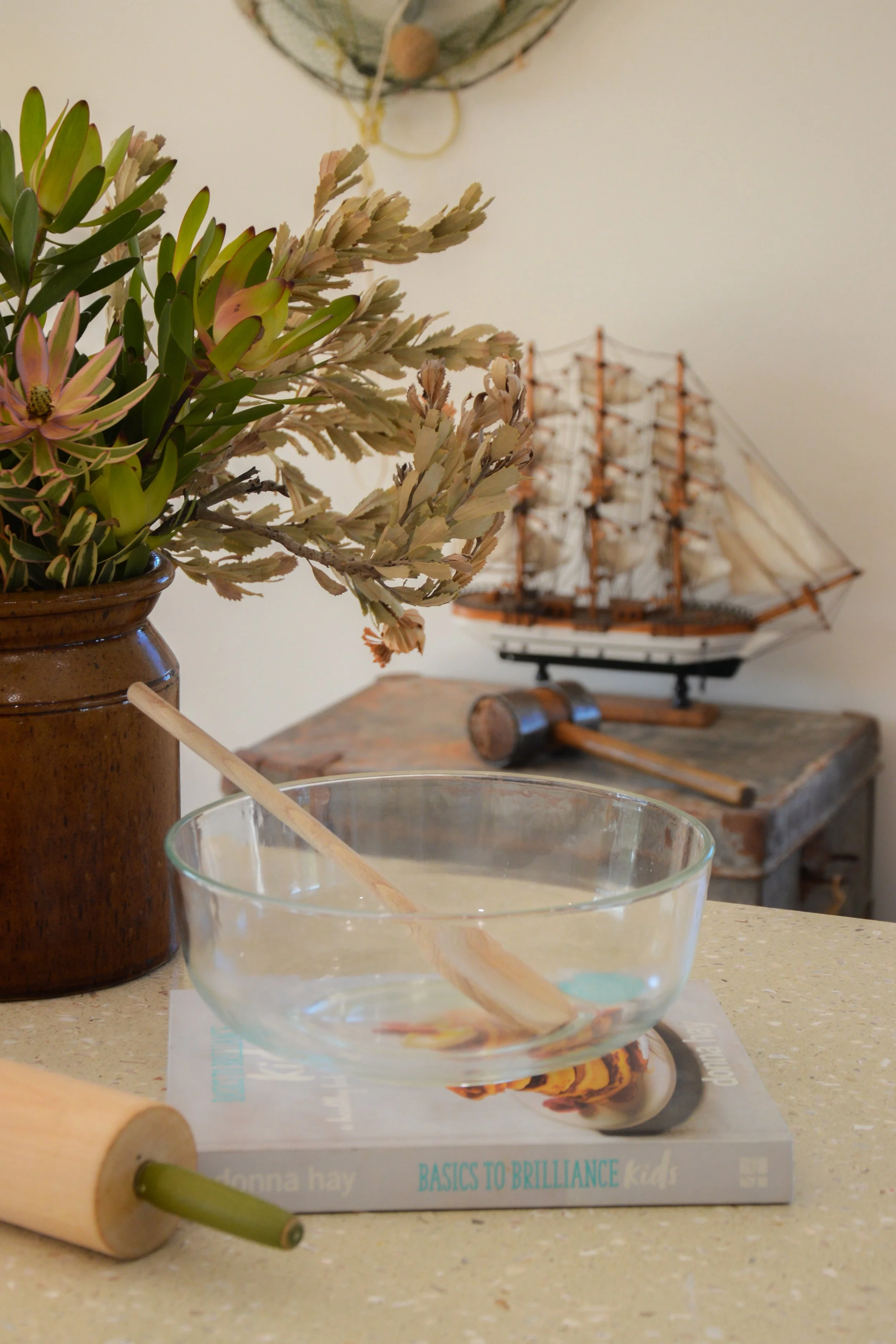 Clear bowl with wooden spoon, sitting on a recipe book on a table.