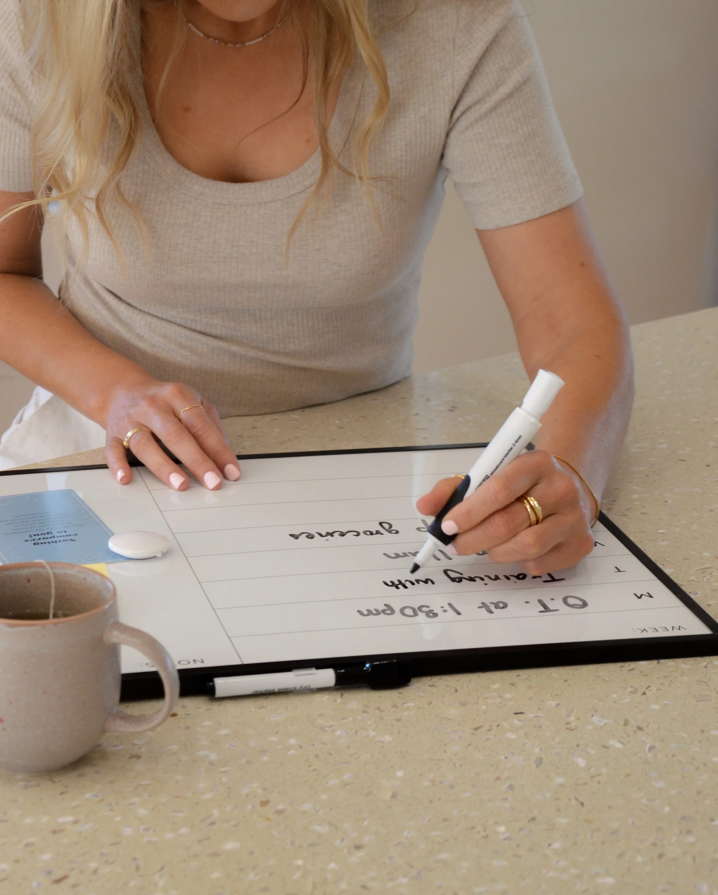 Woman wearing a grey tshirt, writing on a white board with a black texta