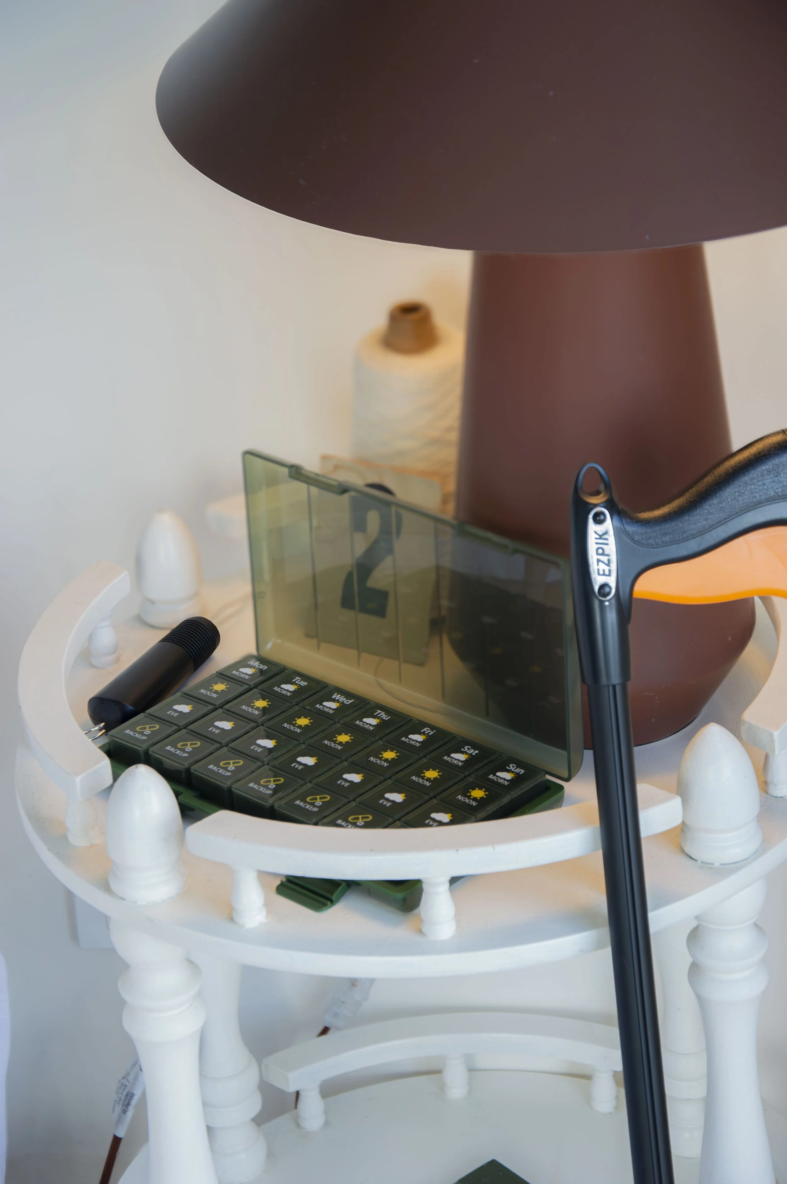 Close-up view of a white wooden table with a lampshade, a portable photo studio light, a small weather forecast board, and several art objects including a conch shell, a white sculpture, and a black flashlight.
