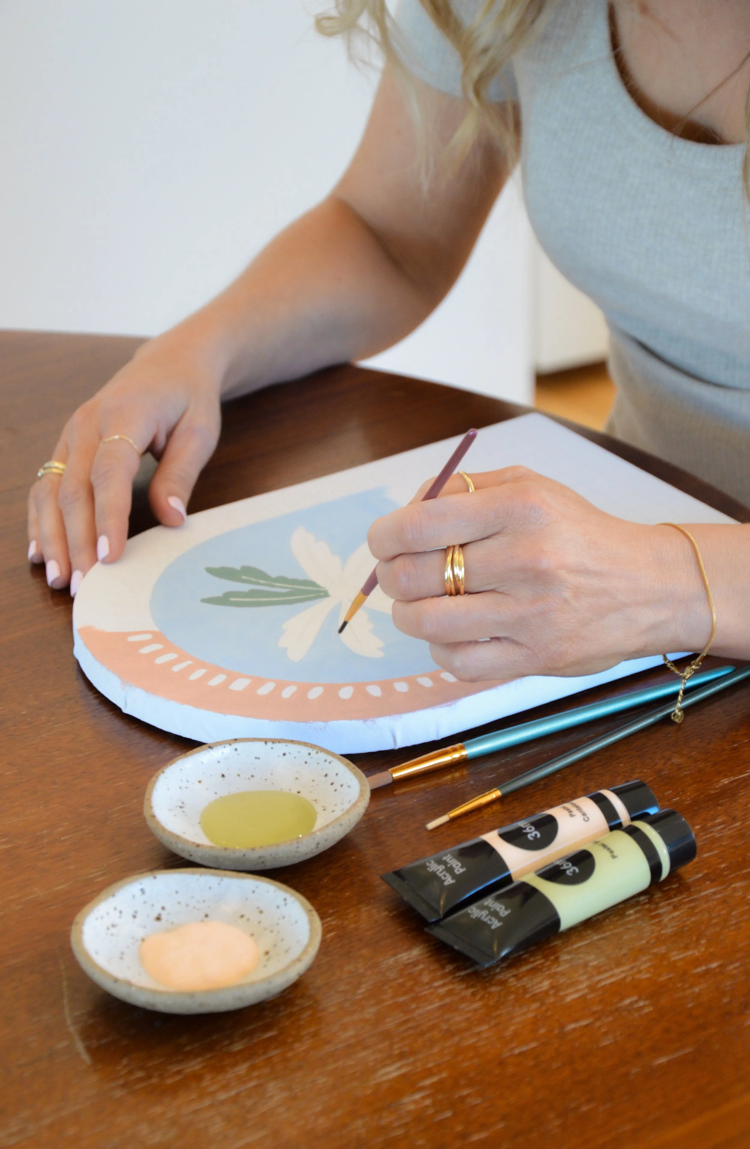 Woman holding paint brush, painting a picture of a palm tree.