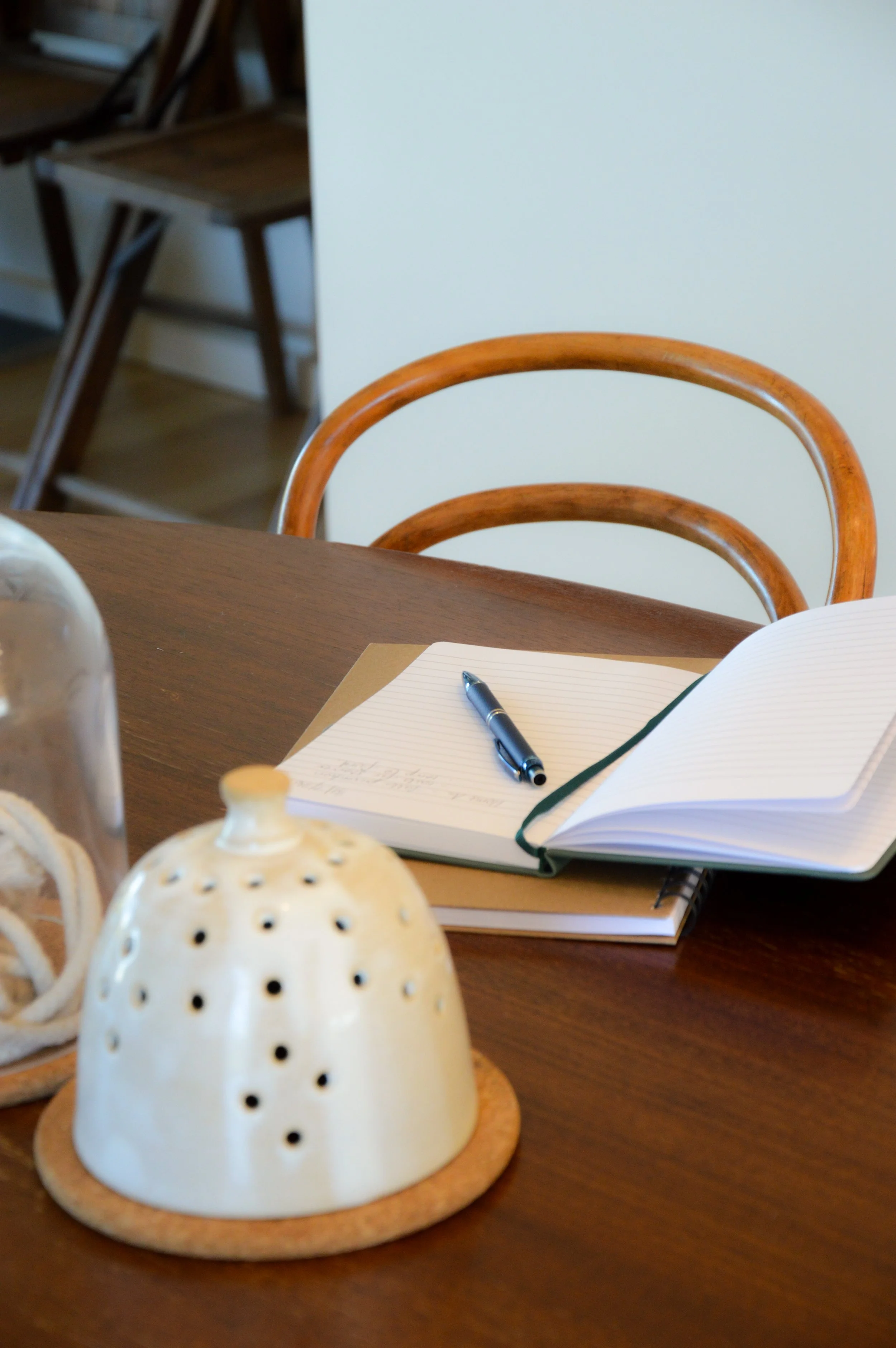 A notebook and pen sitting on a wooden table with a chair in the background.