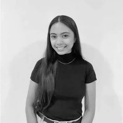 A young woman with long hair wearing a black t-shirt smiling at the camera in front of a plain white background.