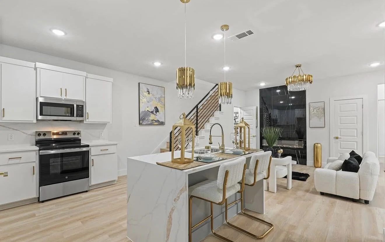 Modern interior of The Colonial model by Echelon Development & Design, featuring an open-concept kitchen and living area with white custom cabinetry, gold accents, a polished marble island, and cozy tailored seating.