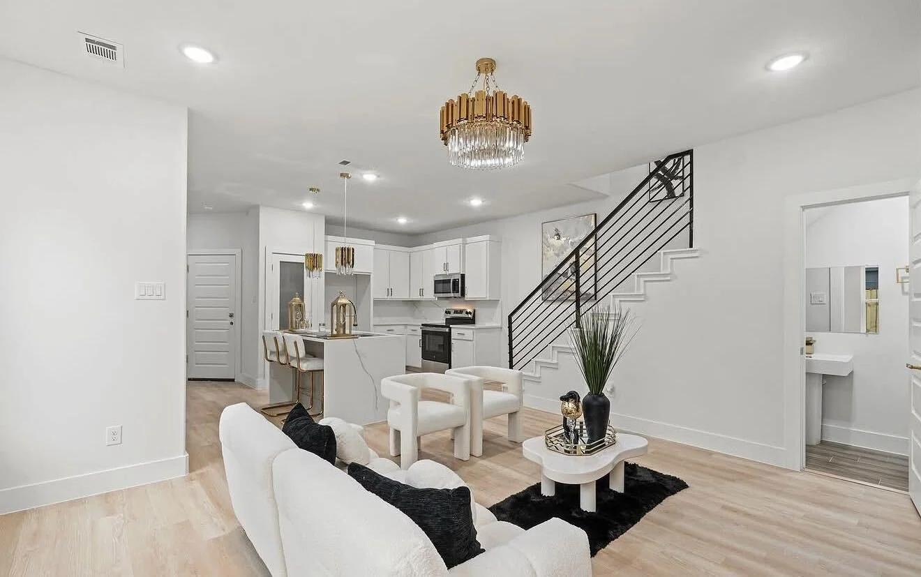 Modern luxury open-concept kitchen featuring clean white cabinetry, polished marble island, gold accent hardware, and an adjacent minimalist seating area.