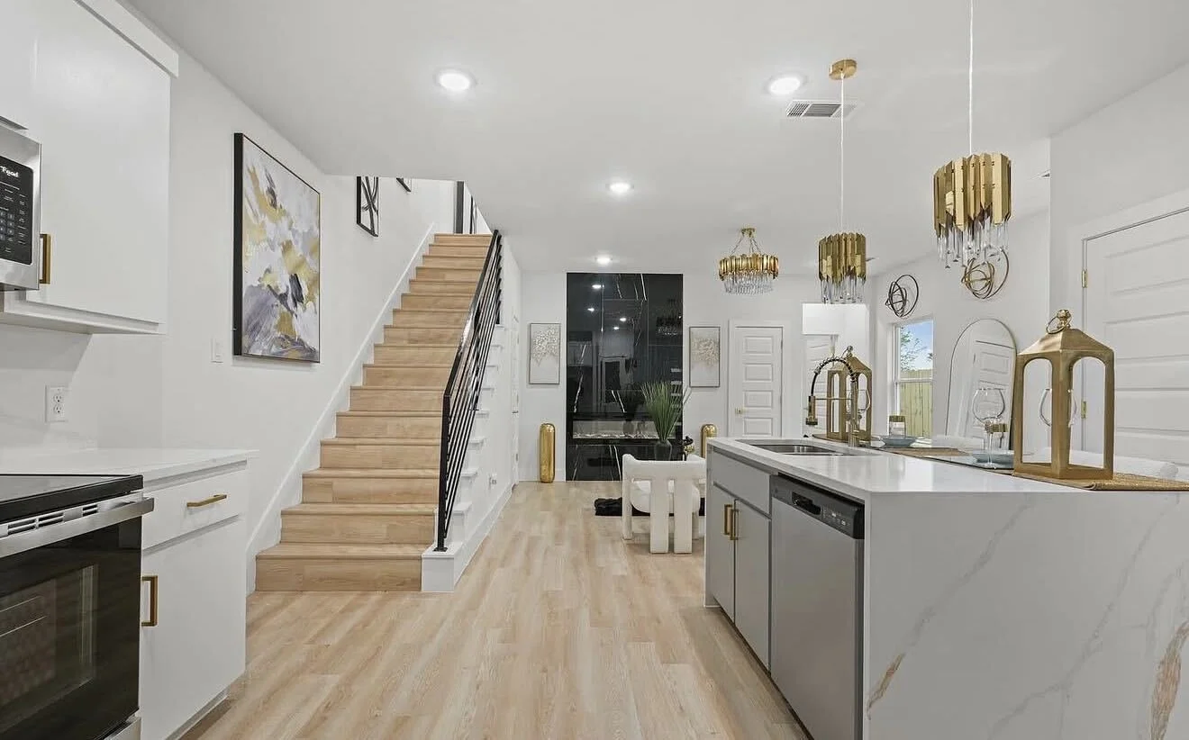 Bright living area and floating staircase interior of The Colonial model by Echelon Development & Design, featuring light hardwood floors, gold accents, and clean architectural lines.