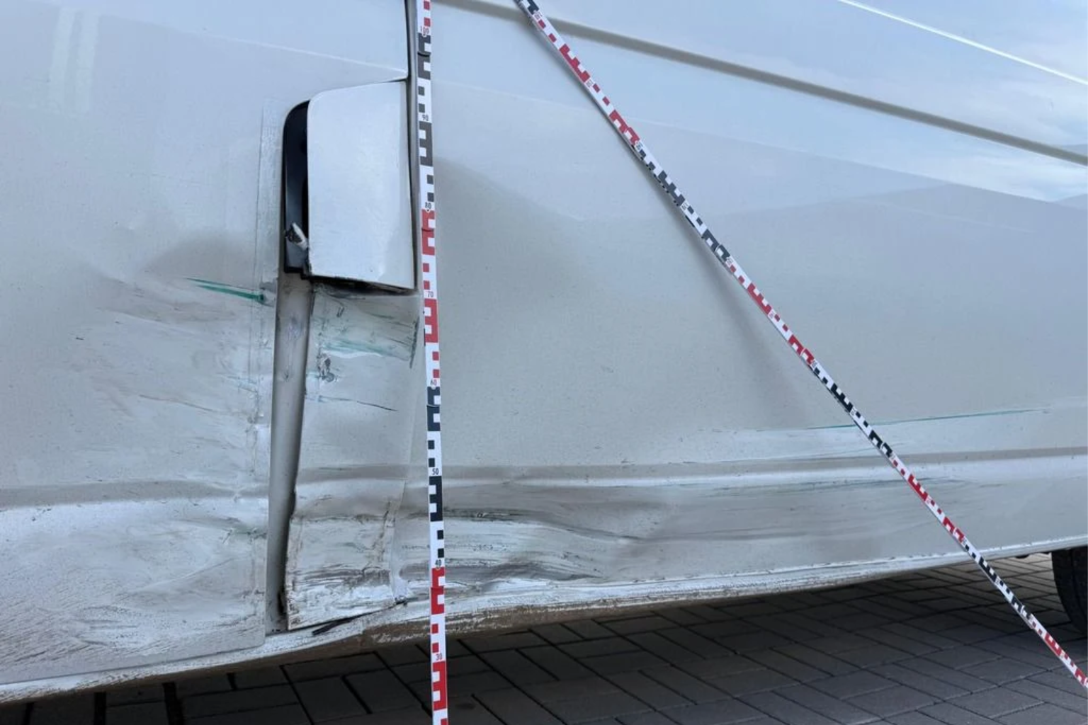 Unfallauto mit beschädigter Fahrertür und seitlicher Beule, mit Messlatten zur Unfallaufnahme