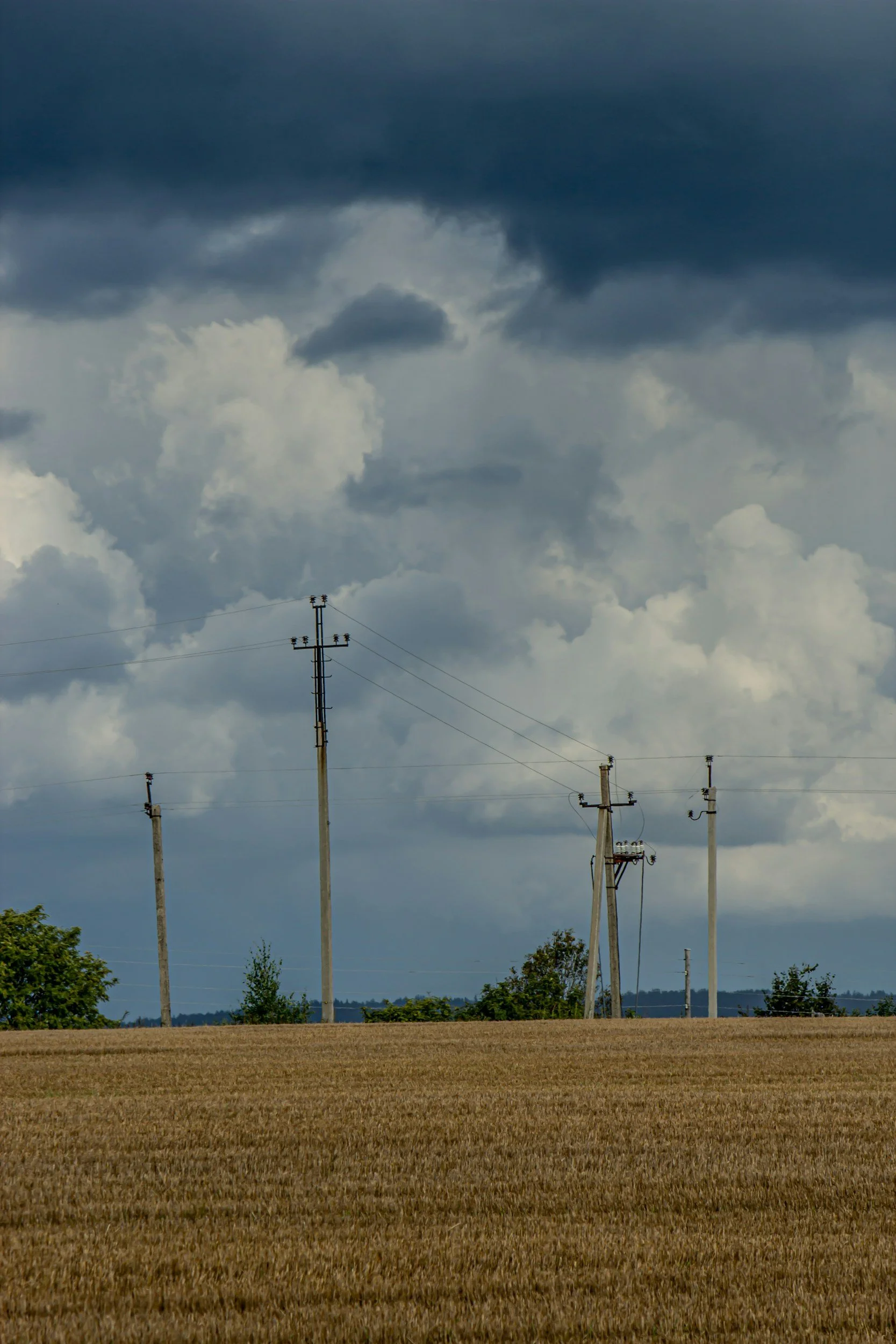 Utility poles and power lines across a harvested field beneath dark storm clouds