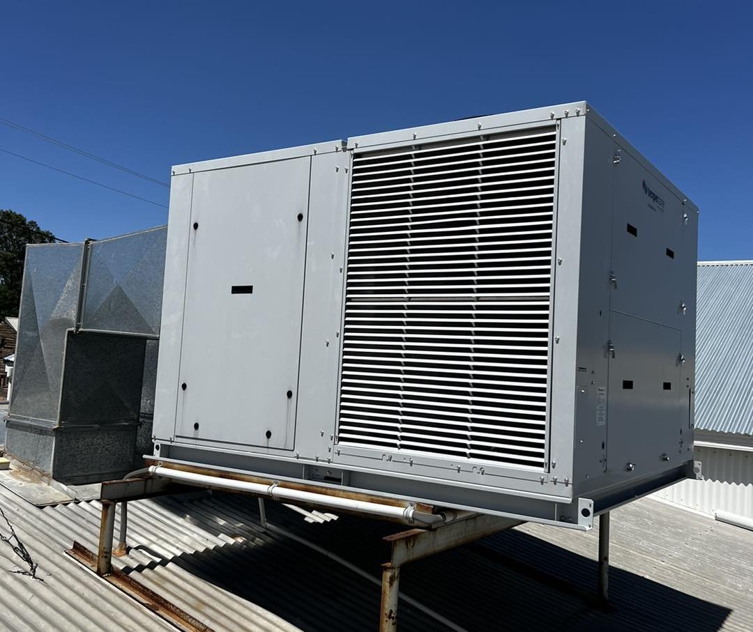 Large rooftop commercial HVAC unit with a protective grille on a metal platform under a clear blue sky