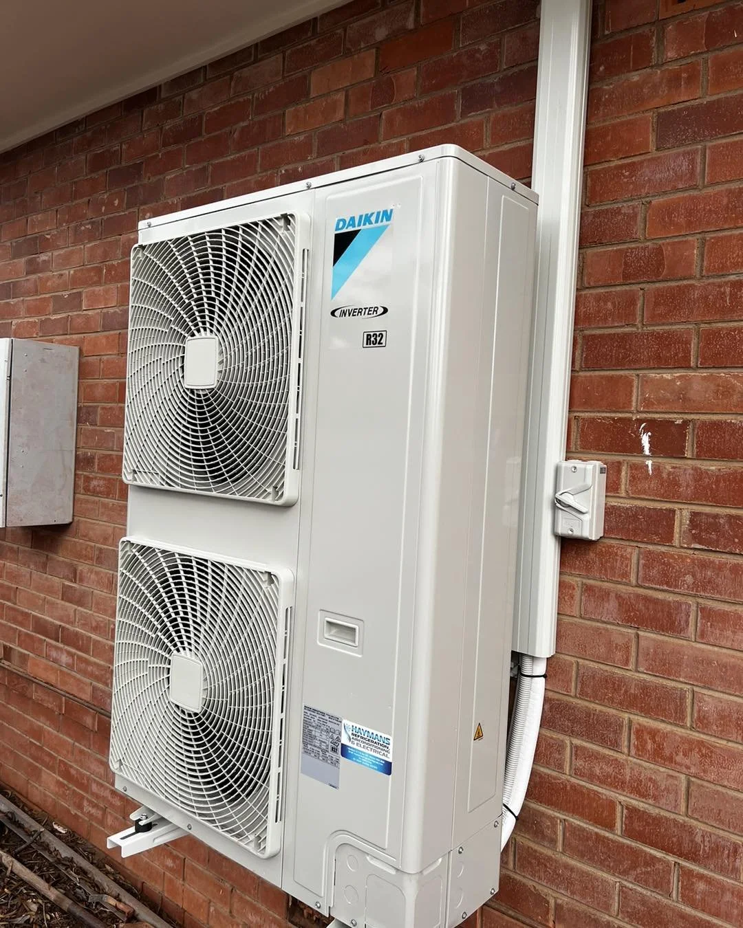 Daikin inverter HVAC outdoor heat pump unit mounted against a red brick wall