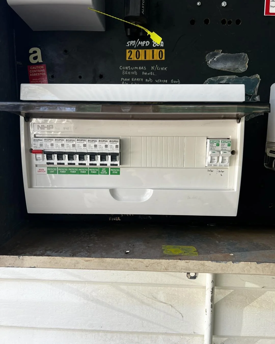 Open residential electrical breaker panel with labeled circuit breakers and an asbestos warning sticker