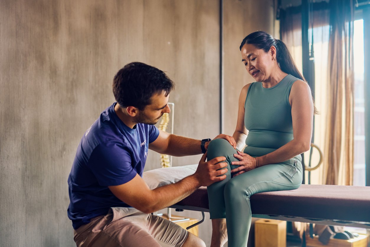 A physical therapist helping an older woman with knee pain in a therapy session in a well-lit room.