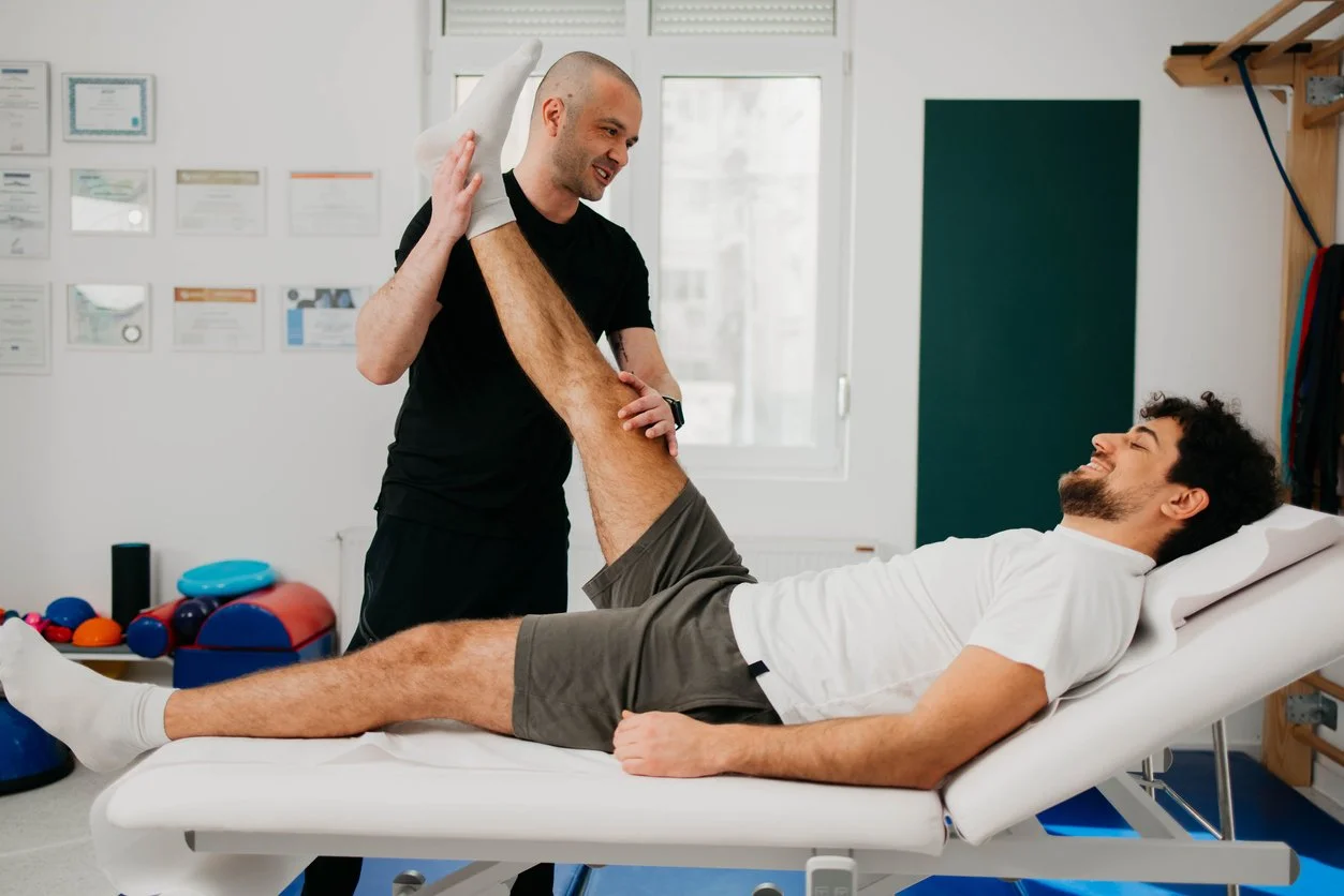 Physical therapist assisting a male patient with leg stretches in a rehabilitation clinic.