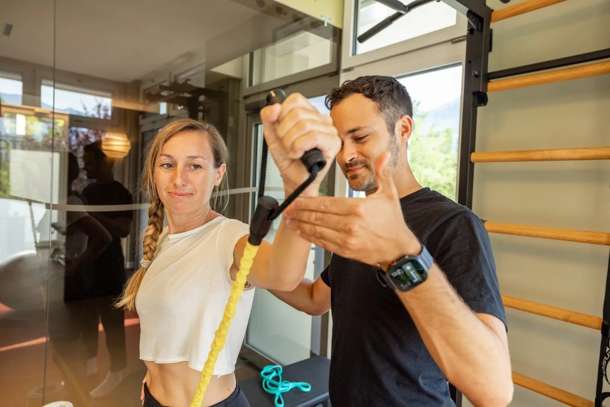 A man helping a woman stretch with a resistance band in a gym.