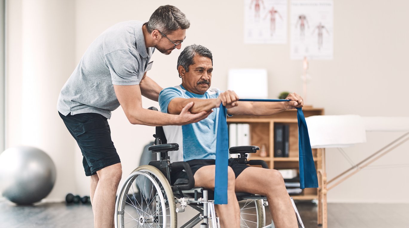 A physical therapist helps a man in a wheelchair stretch with a resistance band in a rehabilitation center.