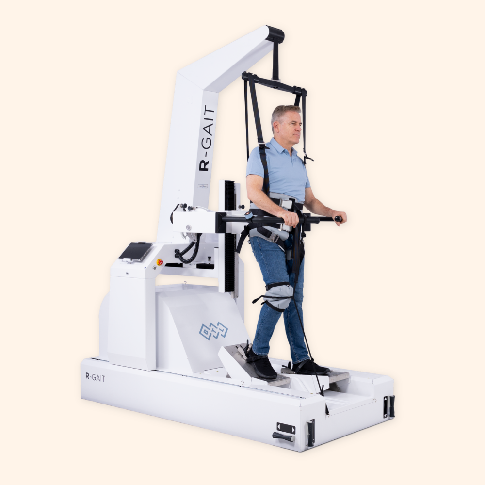 A man standing on a gait training machine with a harness and support system to assist walking rehabilitation.