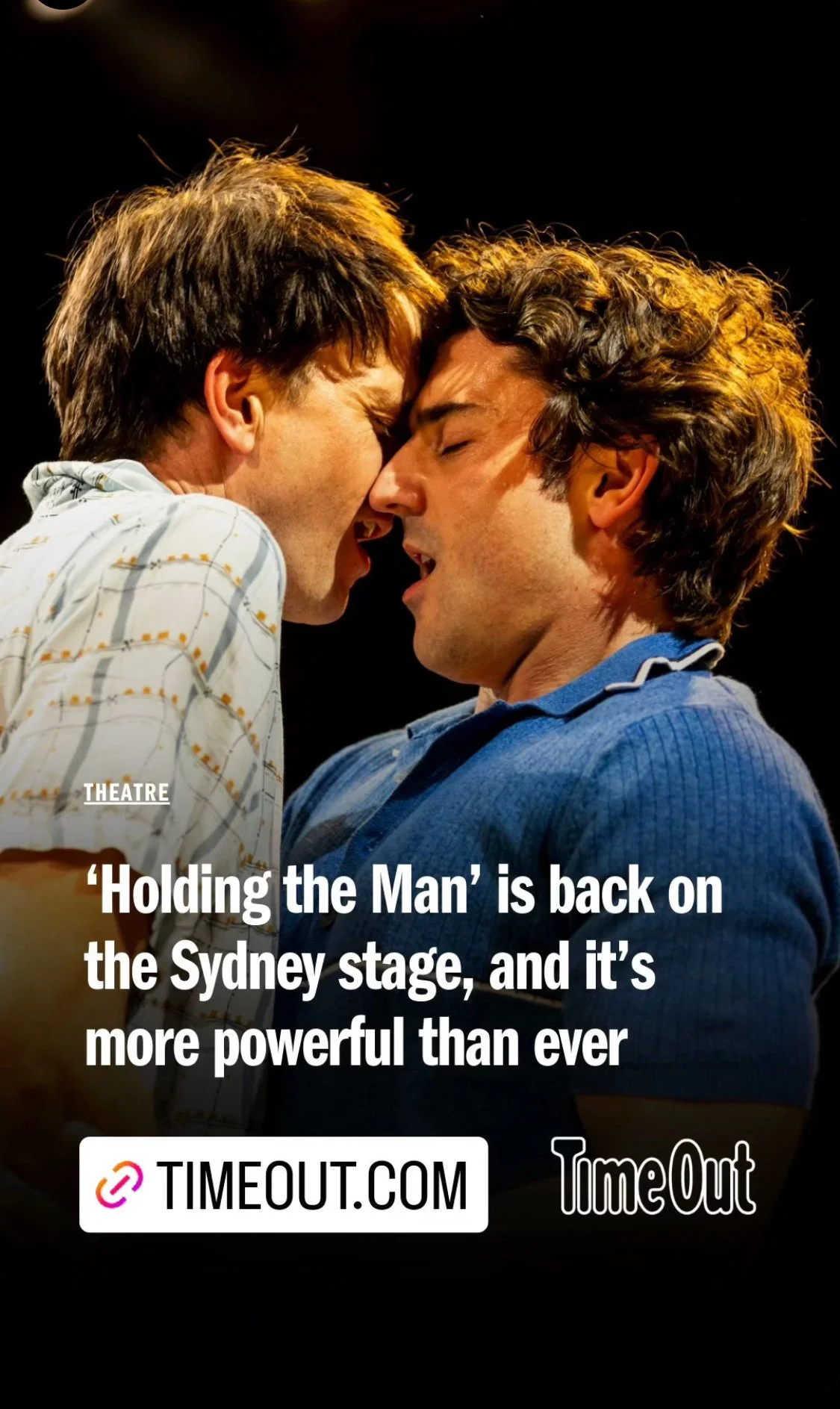 Two actors on stage with faces close together, one with brown hair and the other with curly dark hair, appearing to be in a dramatic scene during a theatrical performance.