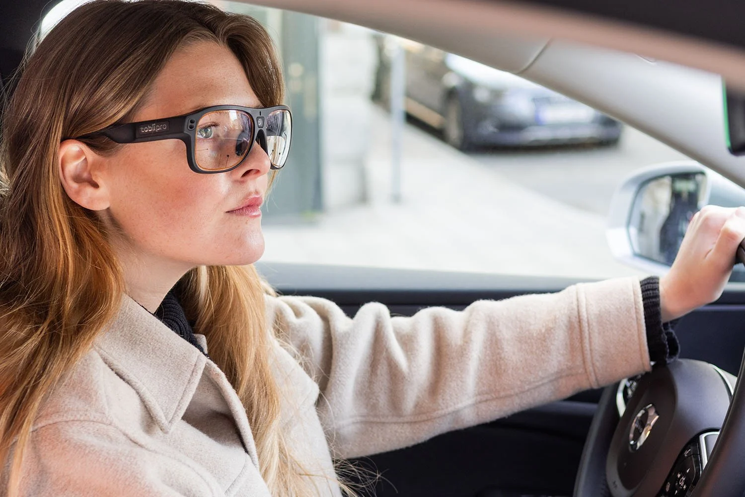A woman with red hair and glasses driving a car.
