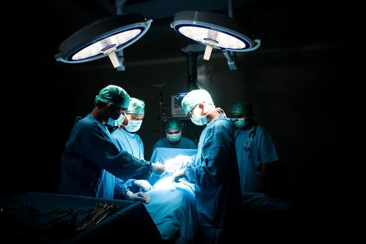 Surgical team performing an operation in an operating room with bright lights overhead.