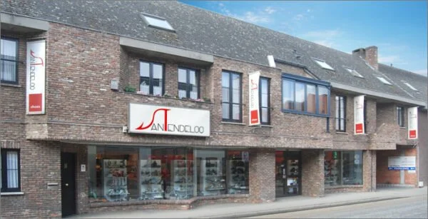 Foto van een stenen winkelpand met grote glazen ramen en een winkelverduistering, vermoedelijk een juwelier of boetiek, met een grote thatched roof en vlaggen aan de gevel.