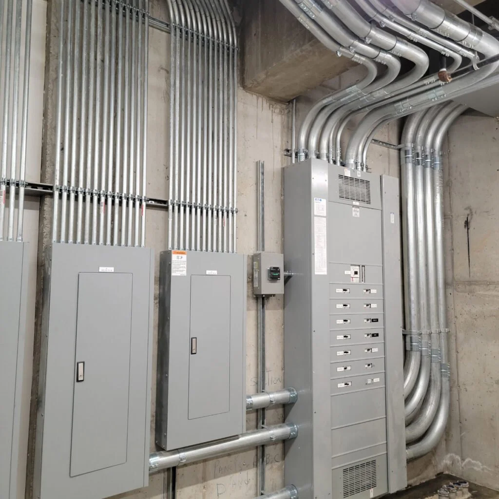 Electrical conduit pipes and control cabinets installed on a concrete wall in a utility or mechanical room.