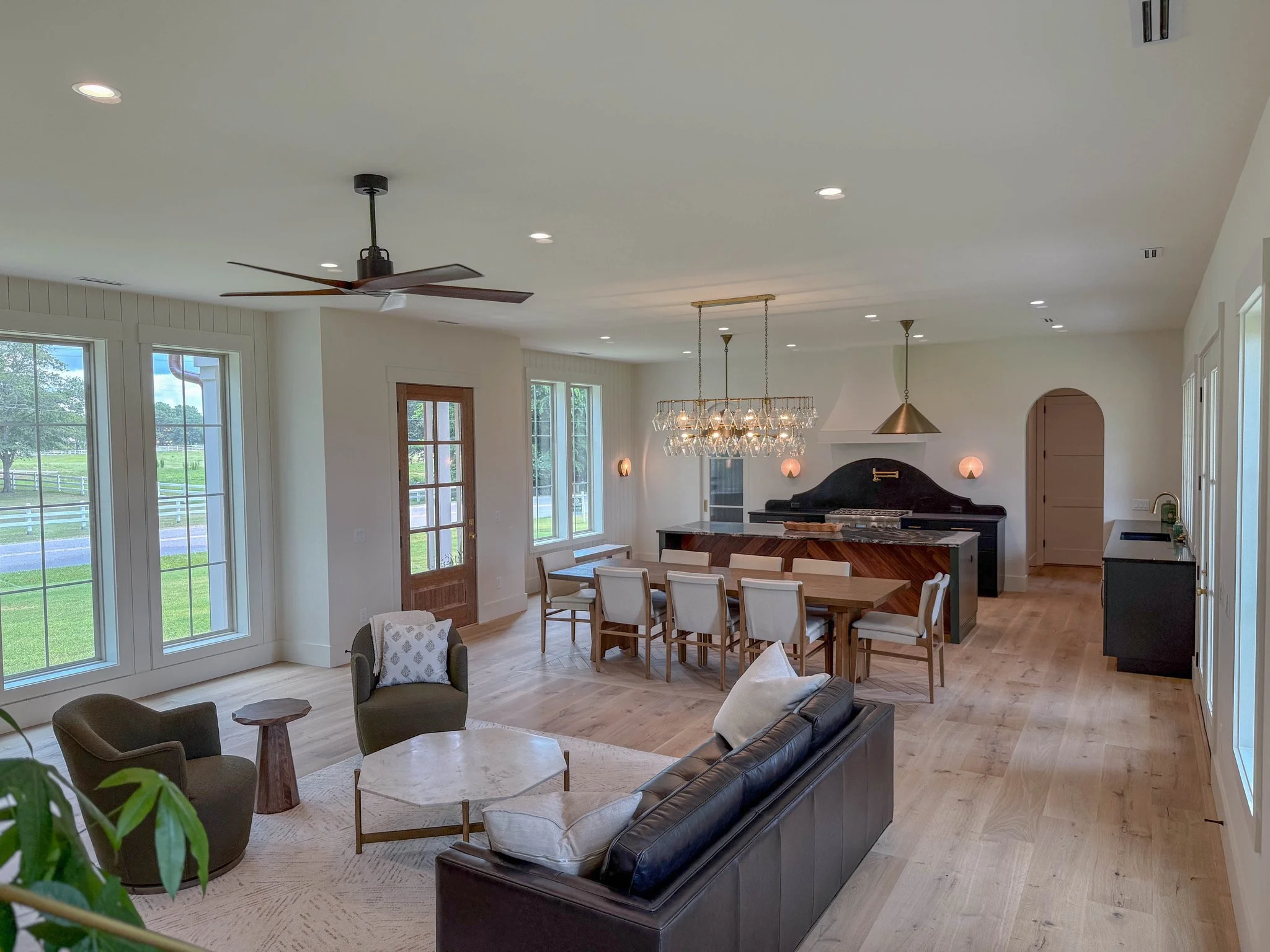 Open concept living and dining area with large windows, modern furniture, a chandelier over the dining table, and a ceiling fan.