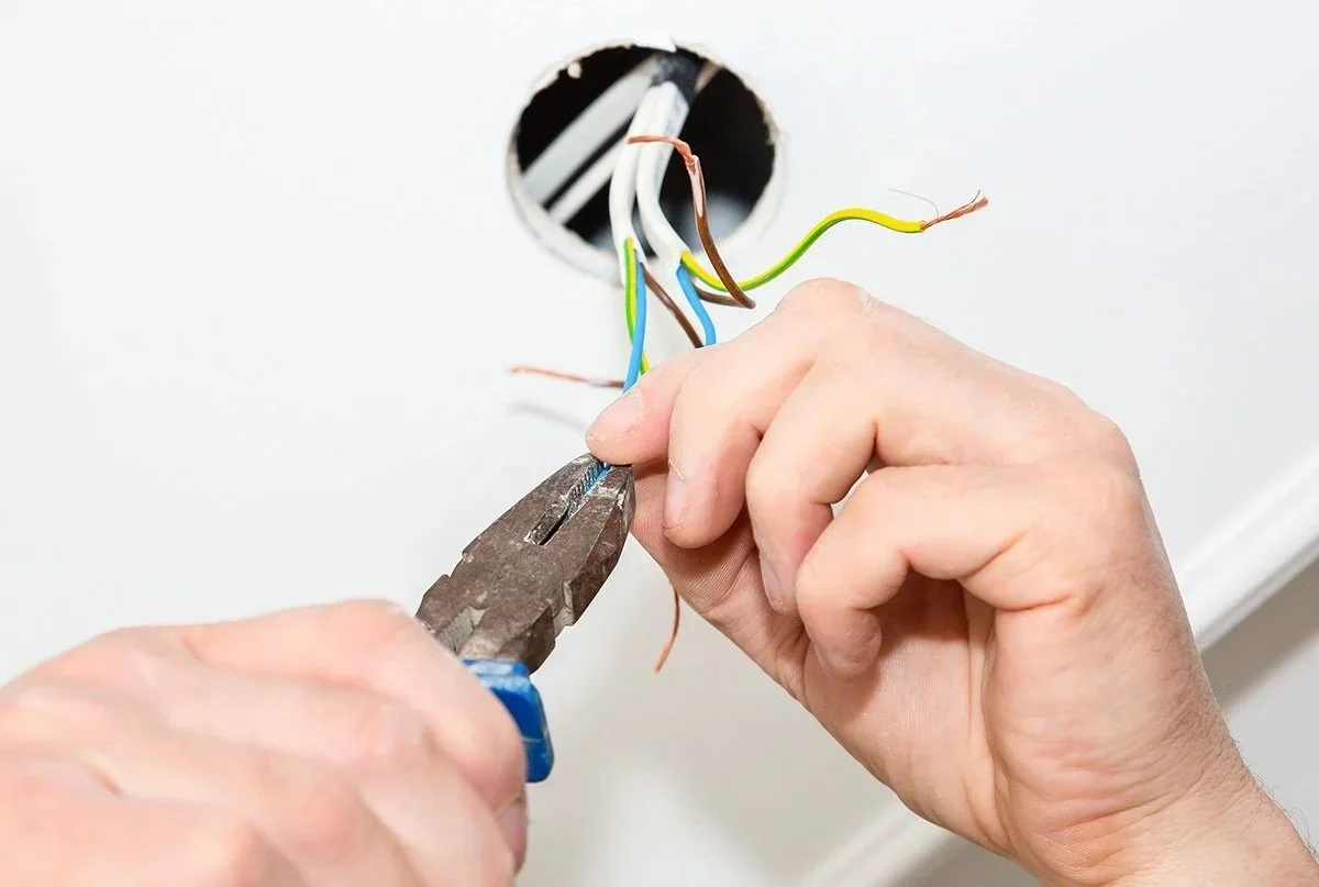Person using pliers to strip wires in an electrical outlet box.