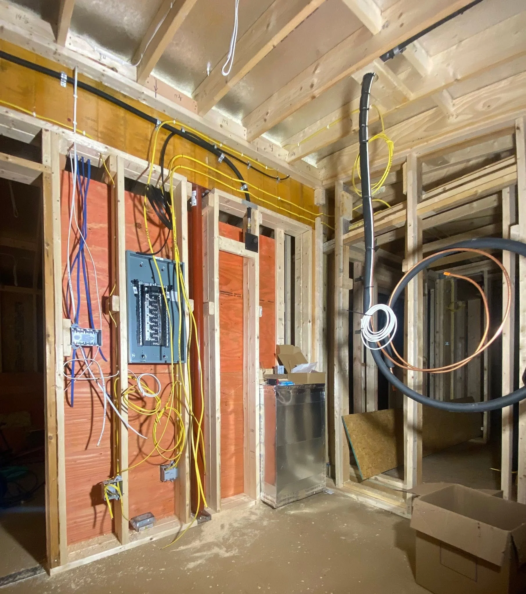 Interior view of a building under construction showing exposed wooden framing, electrical wiring, electrical boxes, and some tools on the floor.