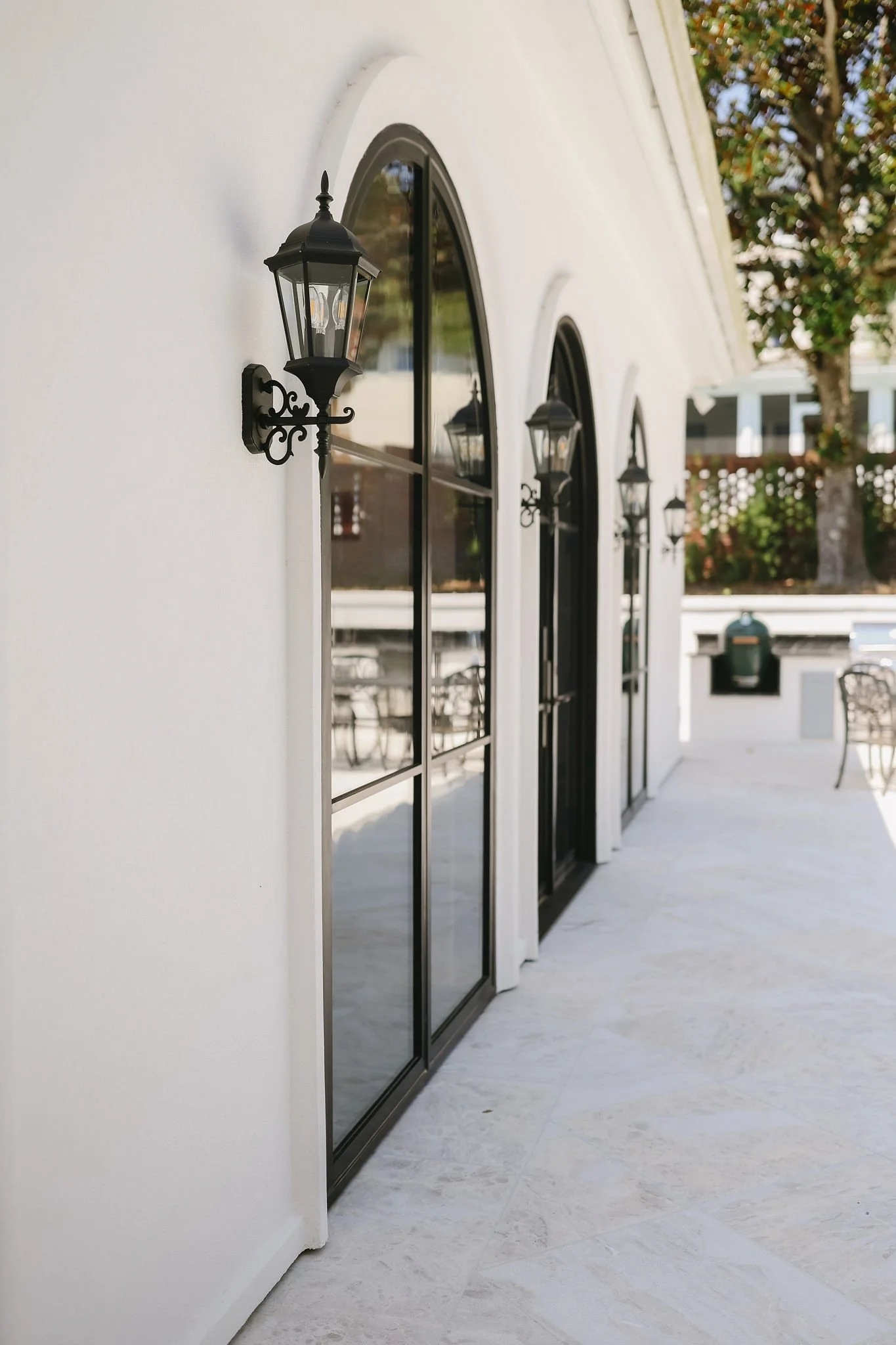 Exterior of a modern white building with black-framed arched windows and black lantern-style light fixtures mounted on the wall.