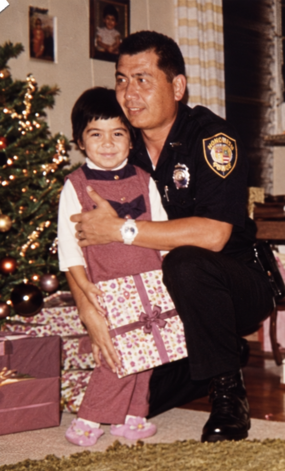Police officer kneeling to hug a young girl by a Christmas tree