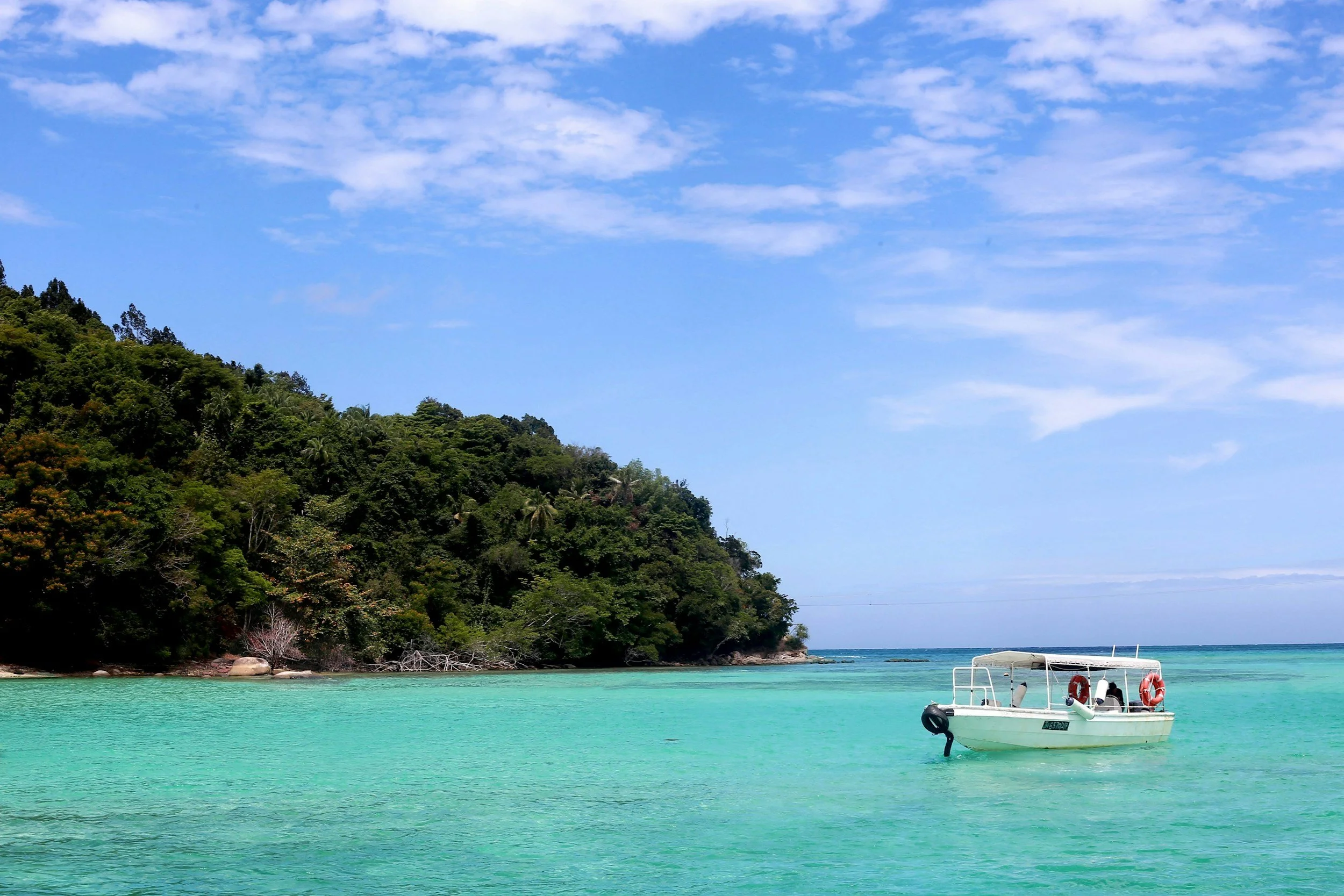 Scenic view of a tropical beach with turquoise water, lush green hillside, and a partly cloudy sky, with a small boat anchored near the shore.