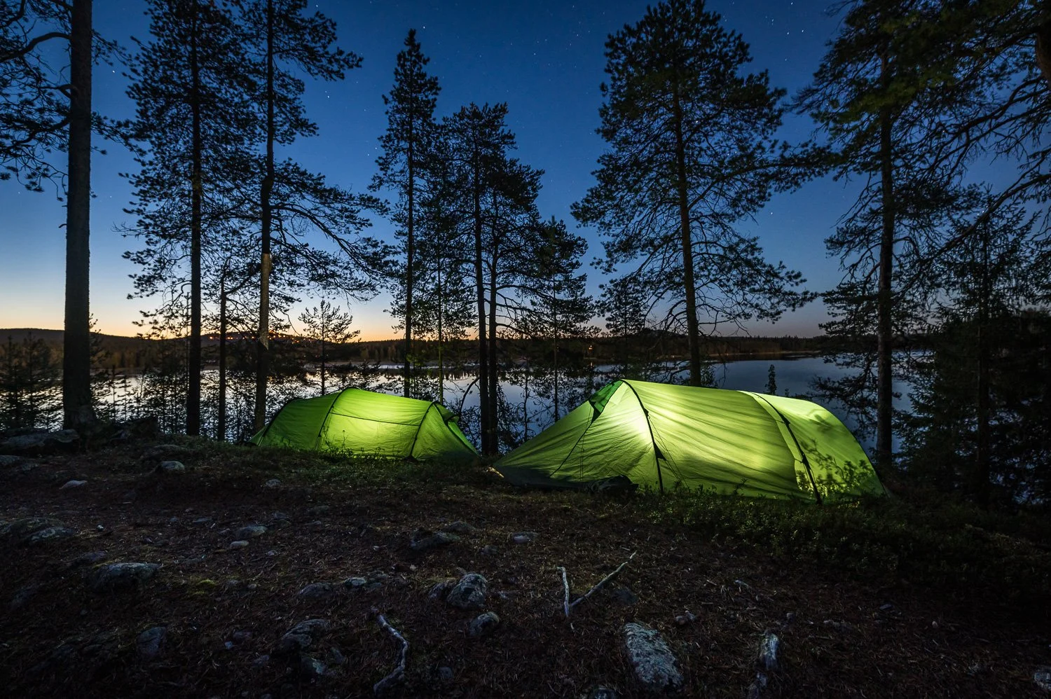 Two green tents pitched near a lake in a forest at dusk