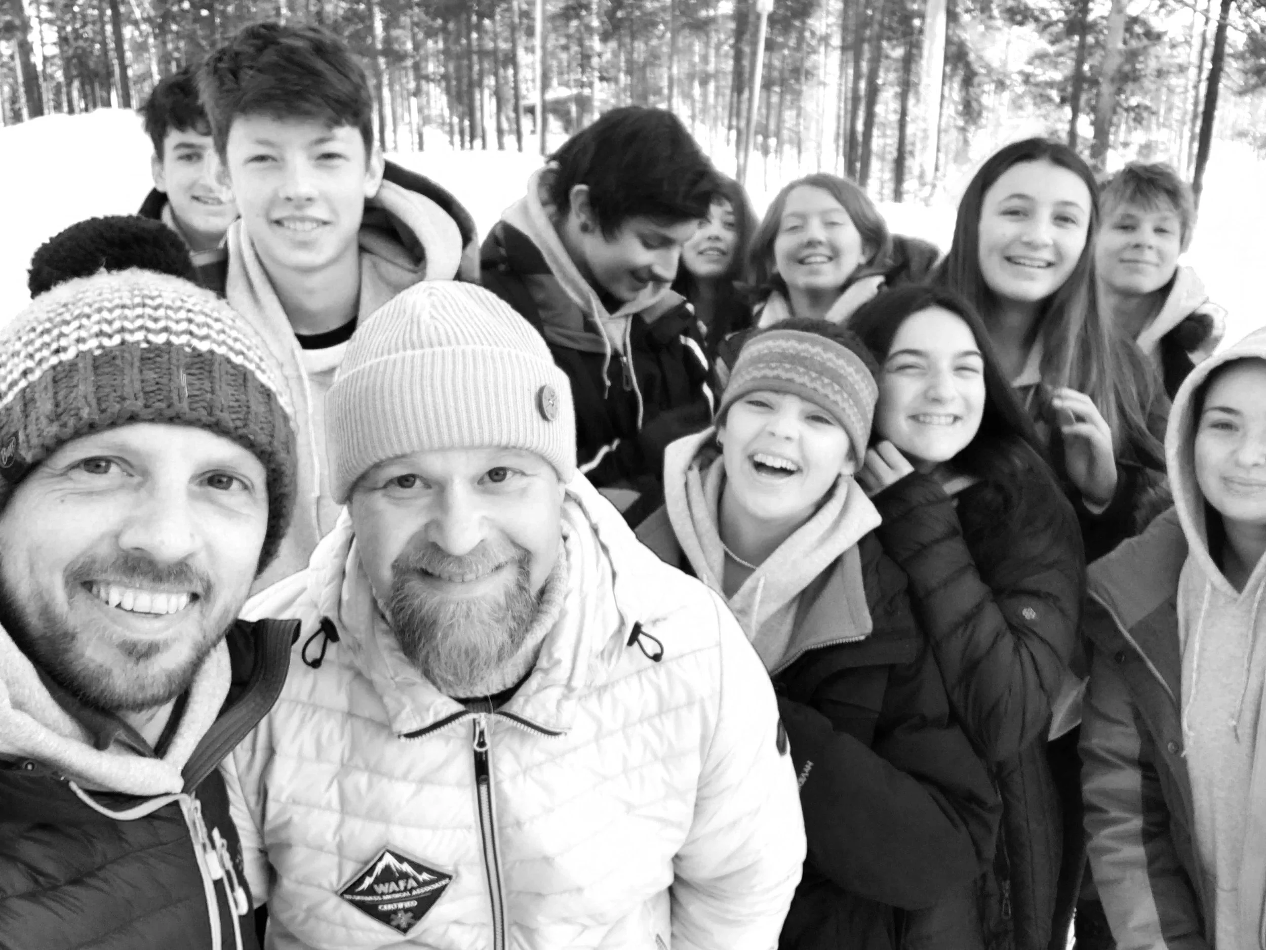 Group of people taking a selfie outdoors in a snowy forest area, dressed in winter clothes.