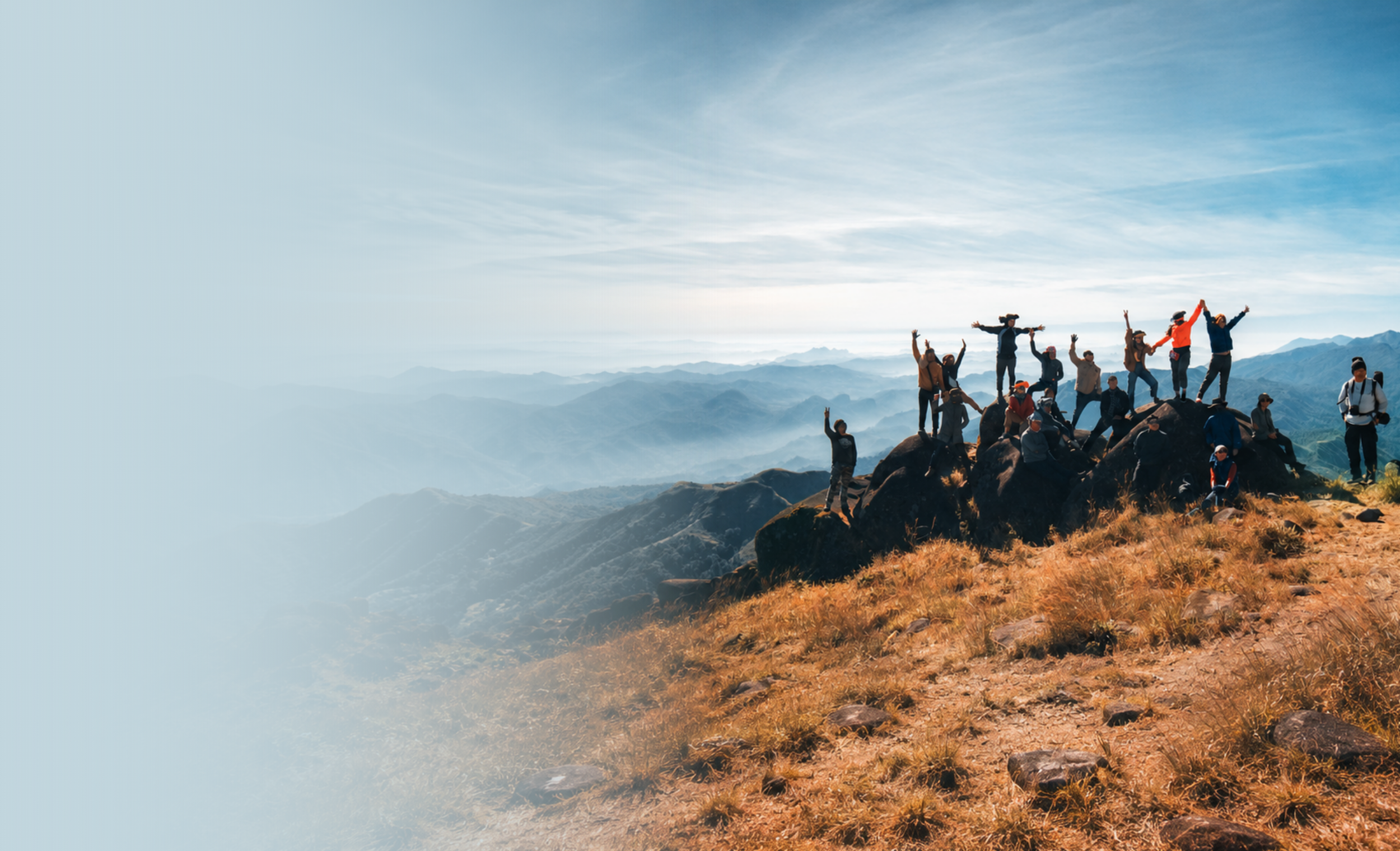 Group of hikers standing on rocky mountain summit with arms raised, overlooking mountain range and sky.