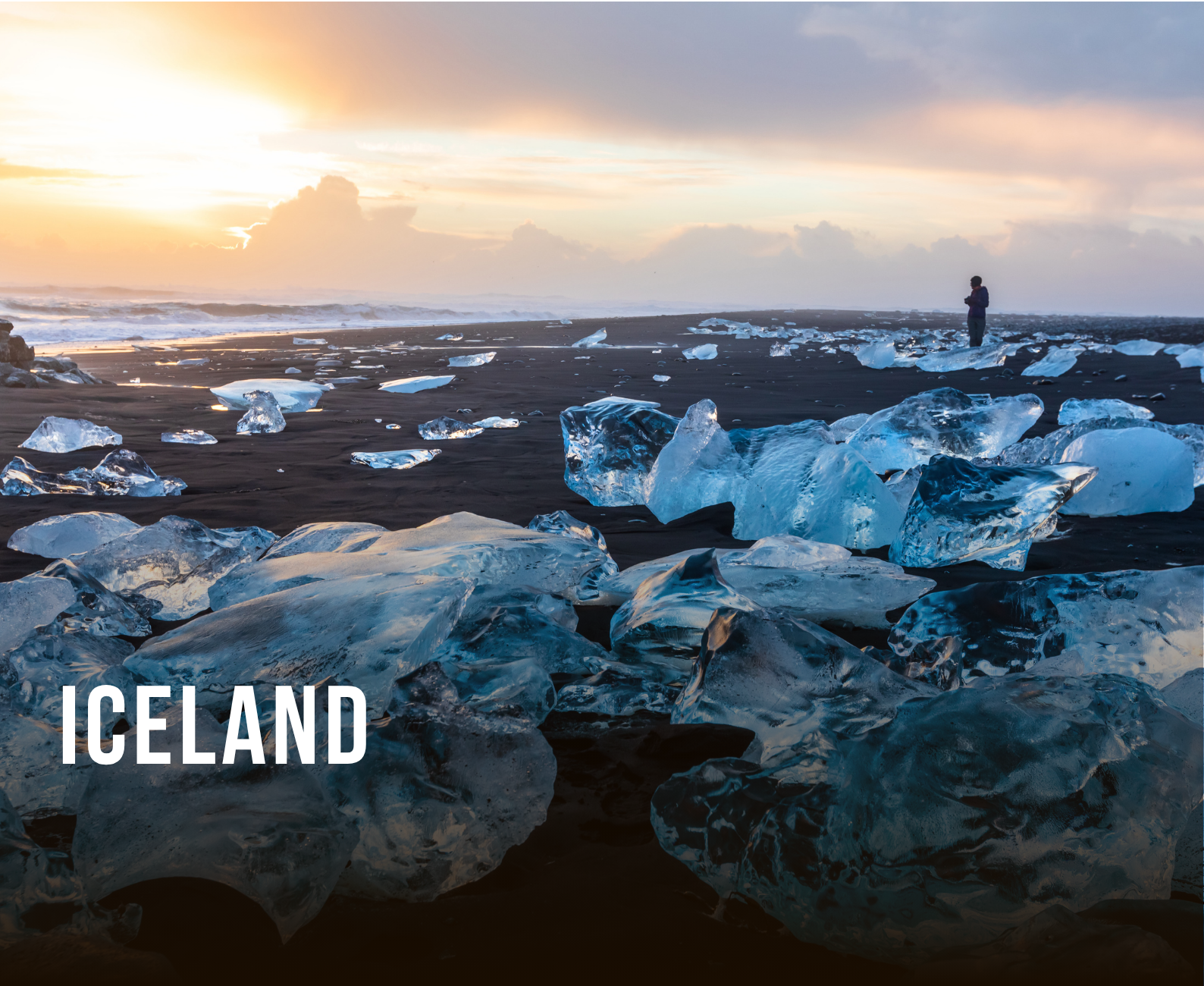 Icelandic black sand beach with scattered ice chunks and a person standing in the distance during sunset.