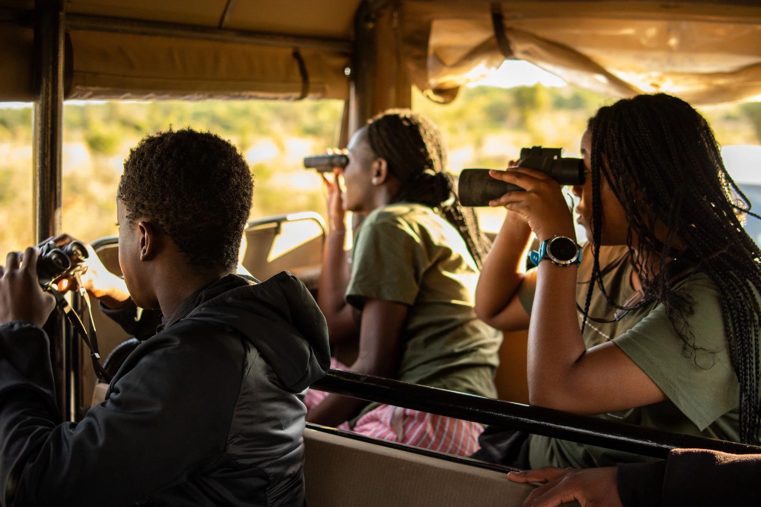 Three women and a man looking through binoculars and a telescope inside a bus, observing the landscape outside.