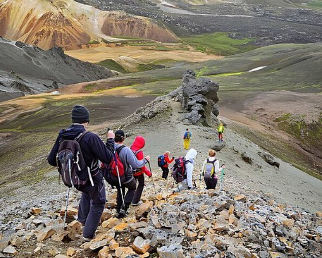 Group of hikers walking down a rocky mountain trail in a volcanic landscape with colorful hills in the background.