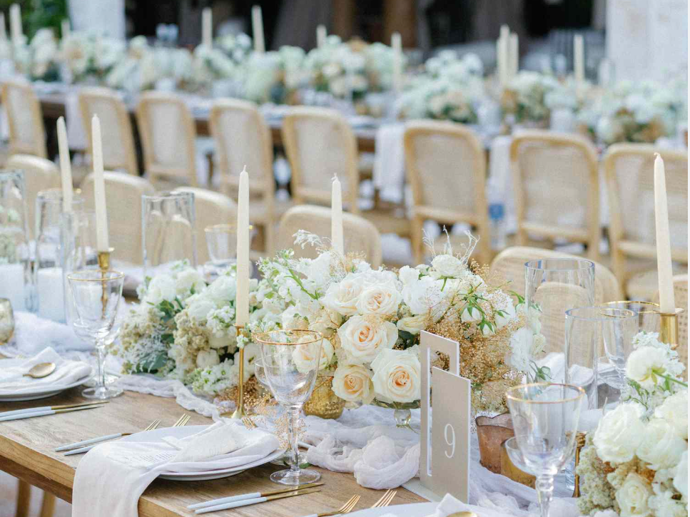 Elegant wedding reception table decorated with white roses, candles, and glassware.