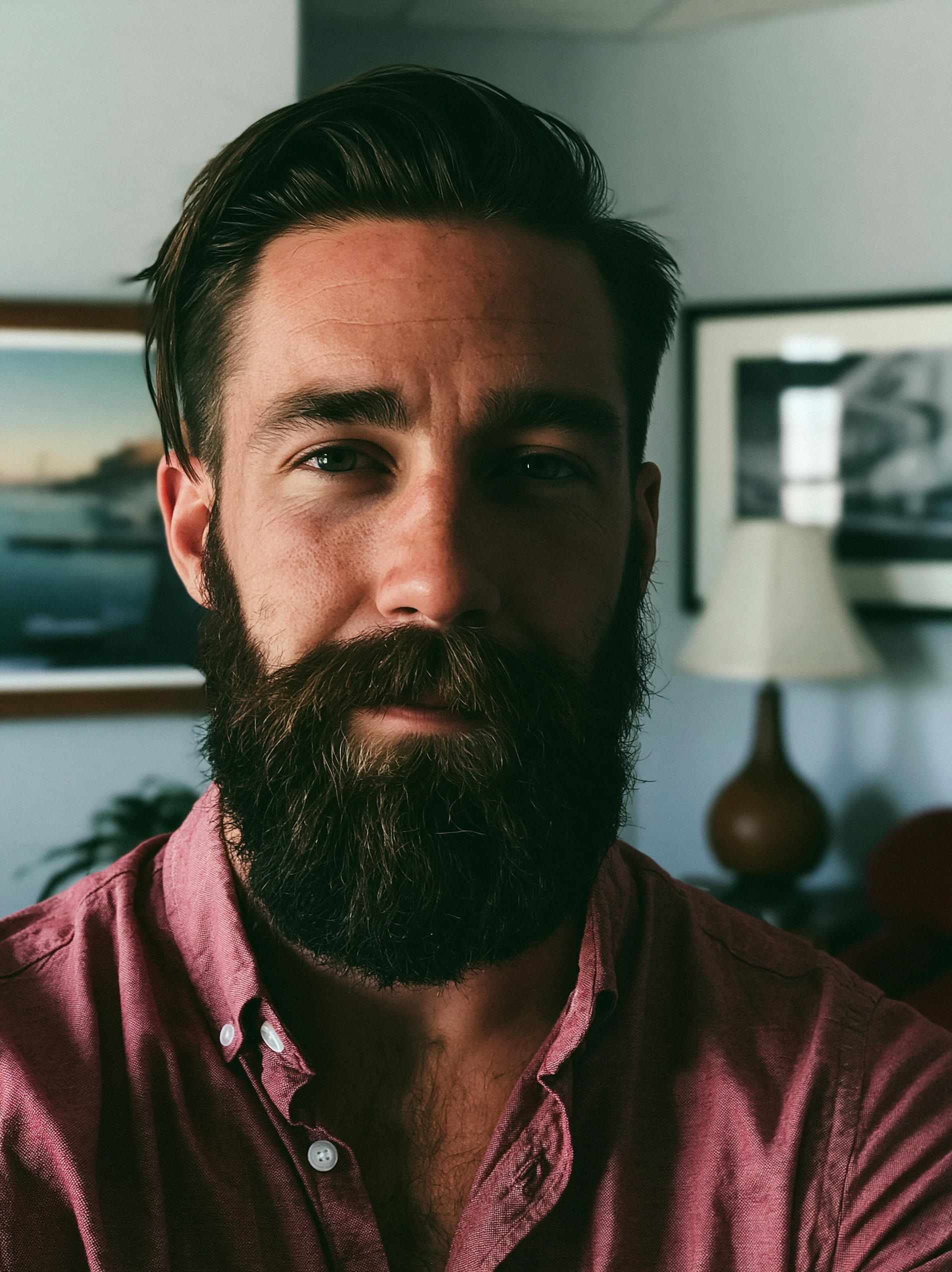 Close-up of a man with dark hair, beard, wearing a maroon shirt, and looking into the camera.