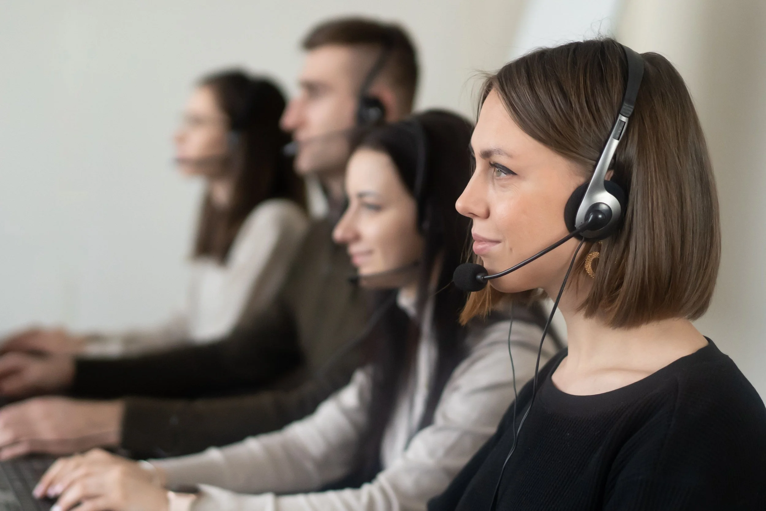 Line of people wearing headsets with microphones, focusing on their tasks.
