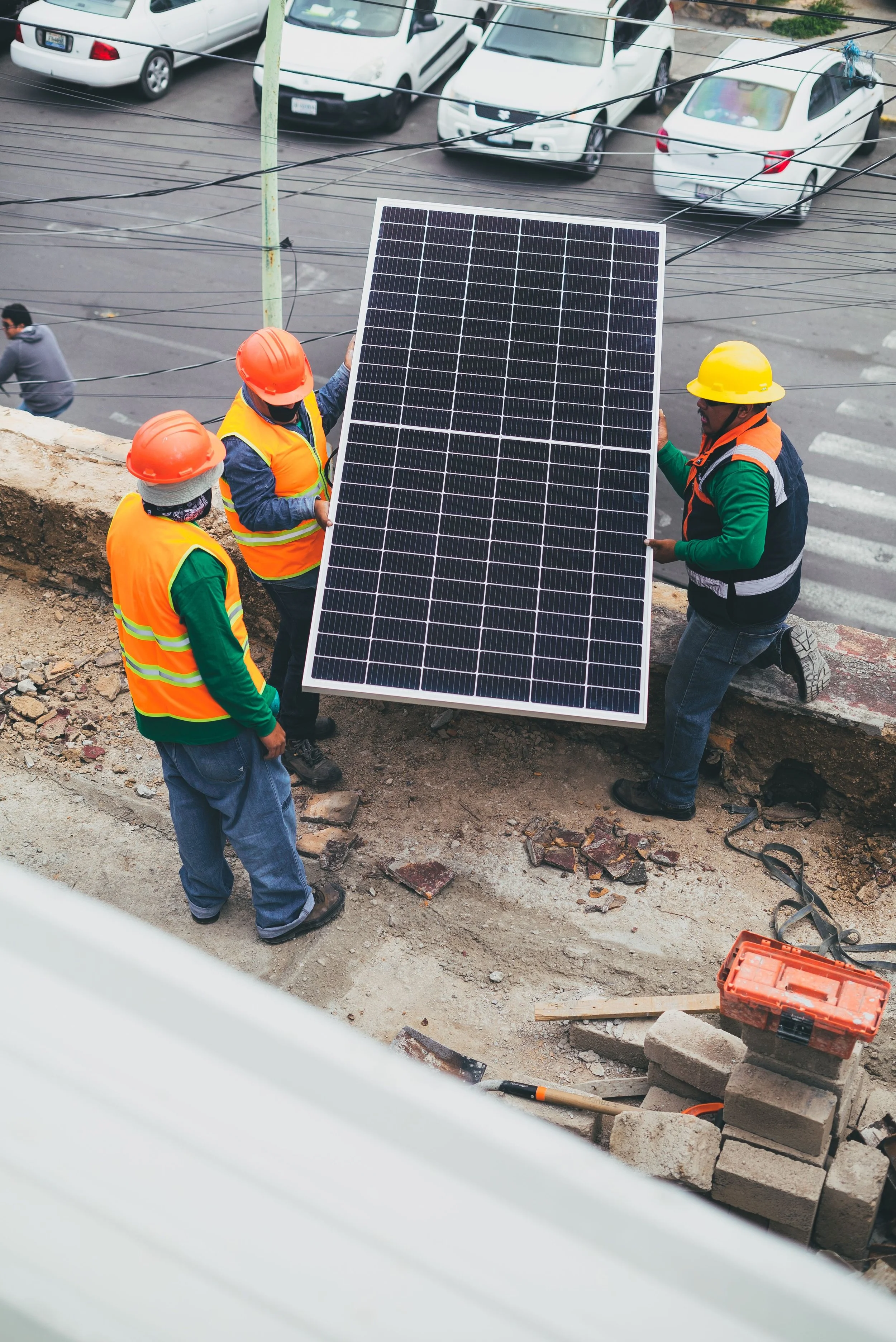 Workers installing solar panels on a construction site near parked cars.